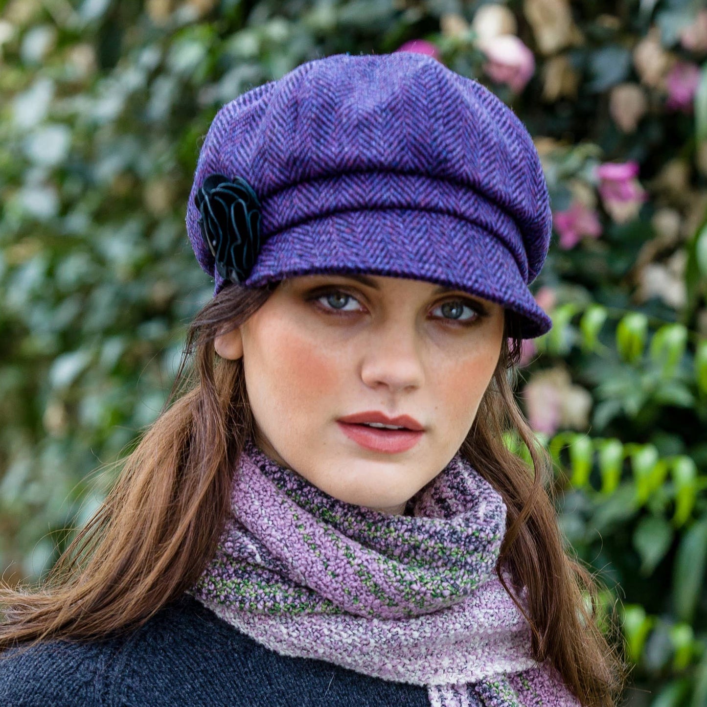 Woman wearing a purple hat and scarf against a green leafy background
