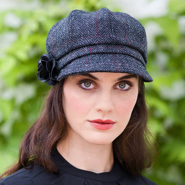Woman wearing a blue checkered hat with a flower against a green leafy background