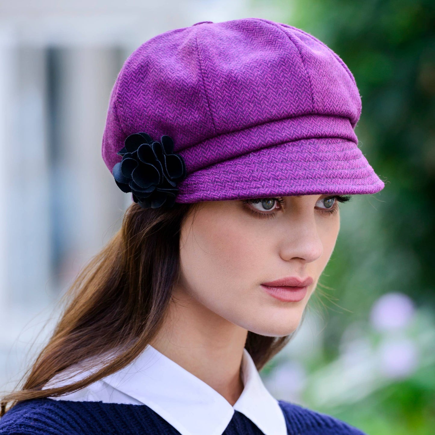 Woman wearing a purple cap with a black flower, standing outdoors.