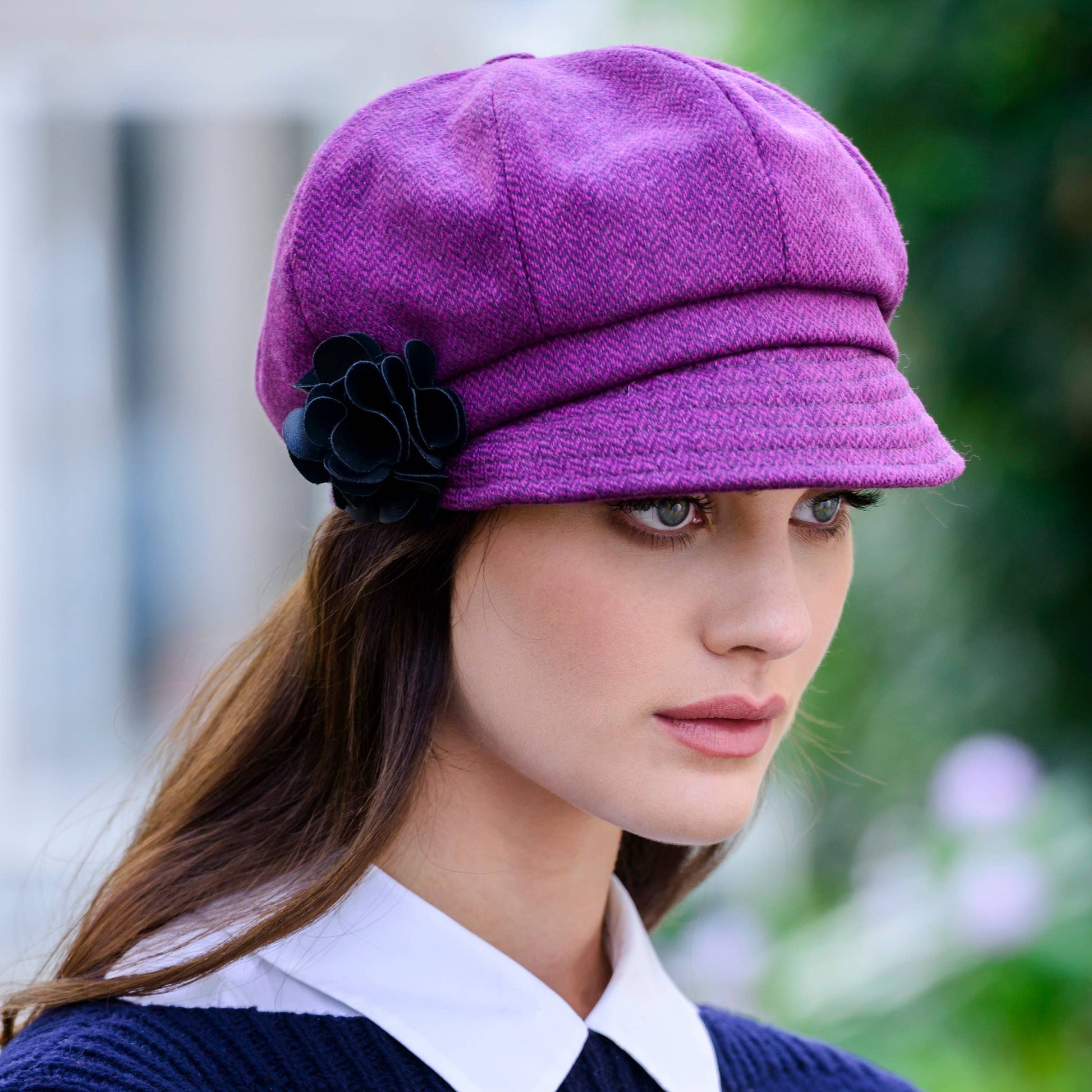 Woman wearing a purple cap with a black flower, standing outdoors.