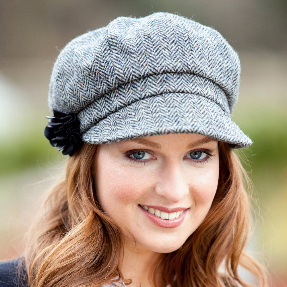 Woman wearing a gray cap with a black flower, outdoors.