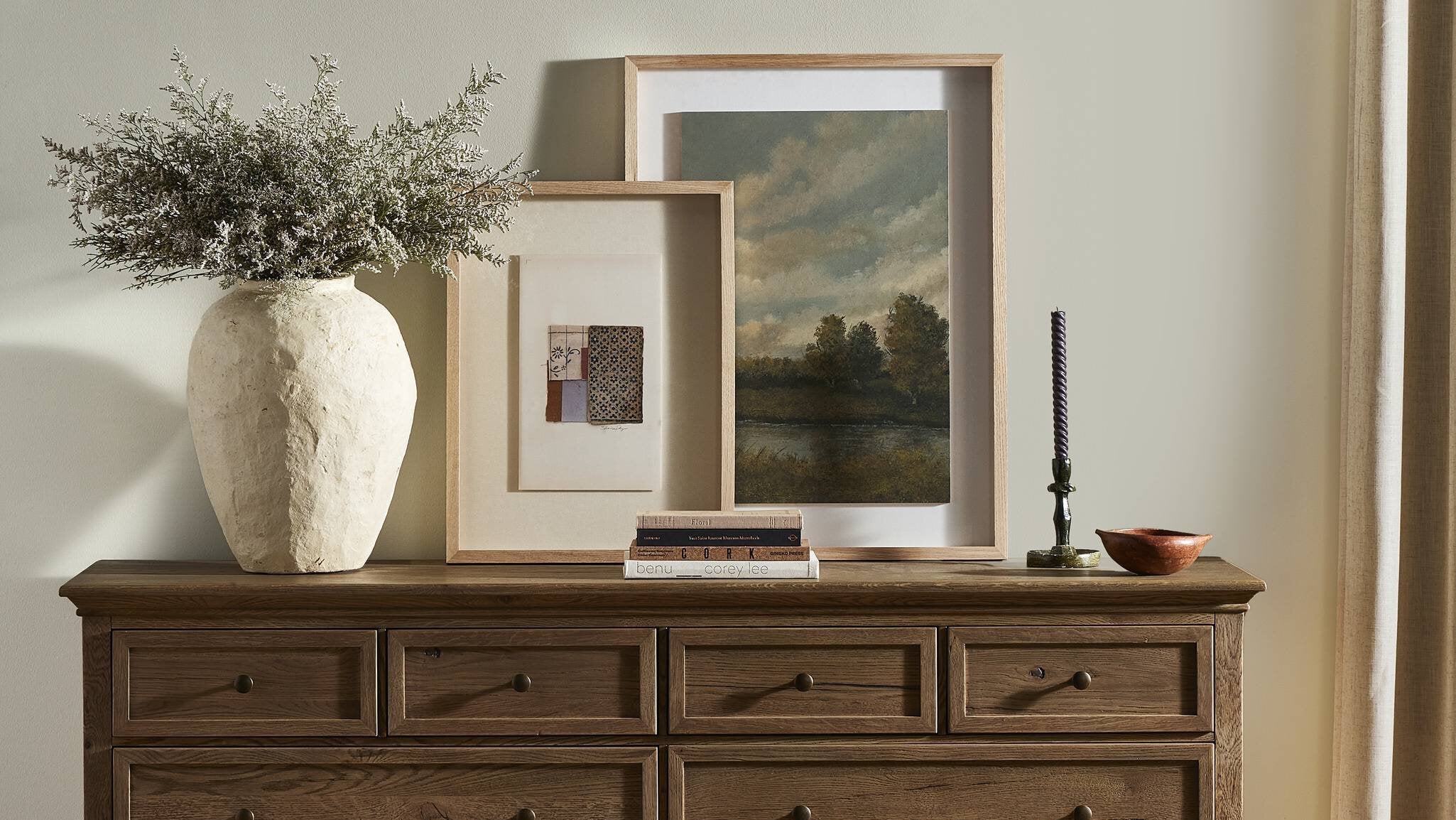 Wooden dresser with decorative items including a vase, framed pictures, and a candle on a neutral background.