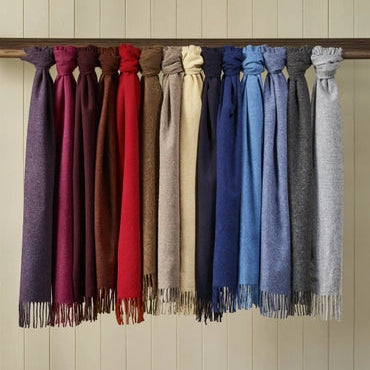 Row of scarves in various colors hanging on a rack against a wooden panel wall.